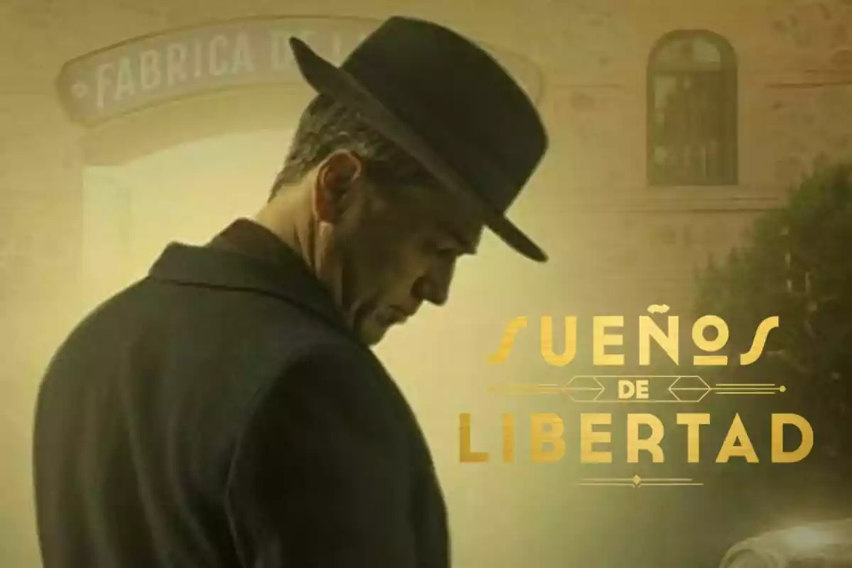 Oriol Tarrasón con sombrero inclina la cabeza frente a un edificio con un cartel que dice "Sueños de Libertad".