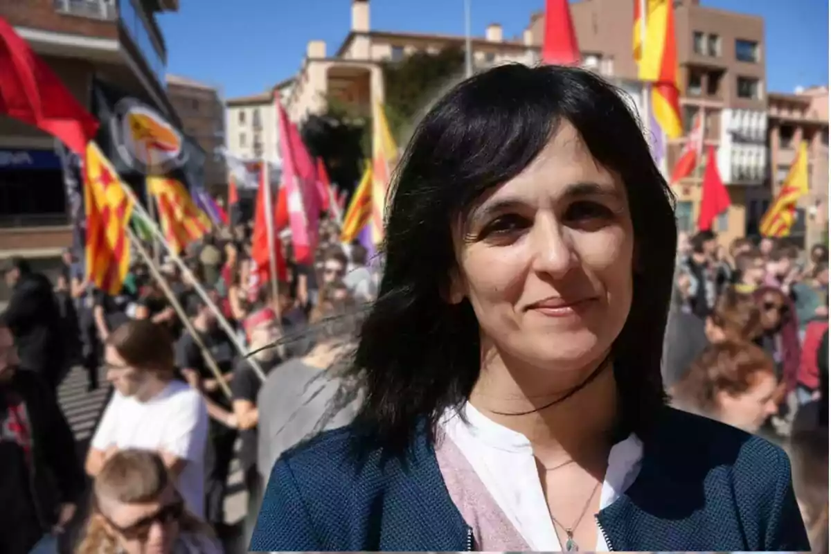 Una dona somrient en primer pla amb una multitud i banderes de fons en un dia assolellat.