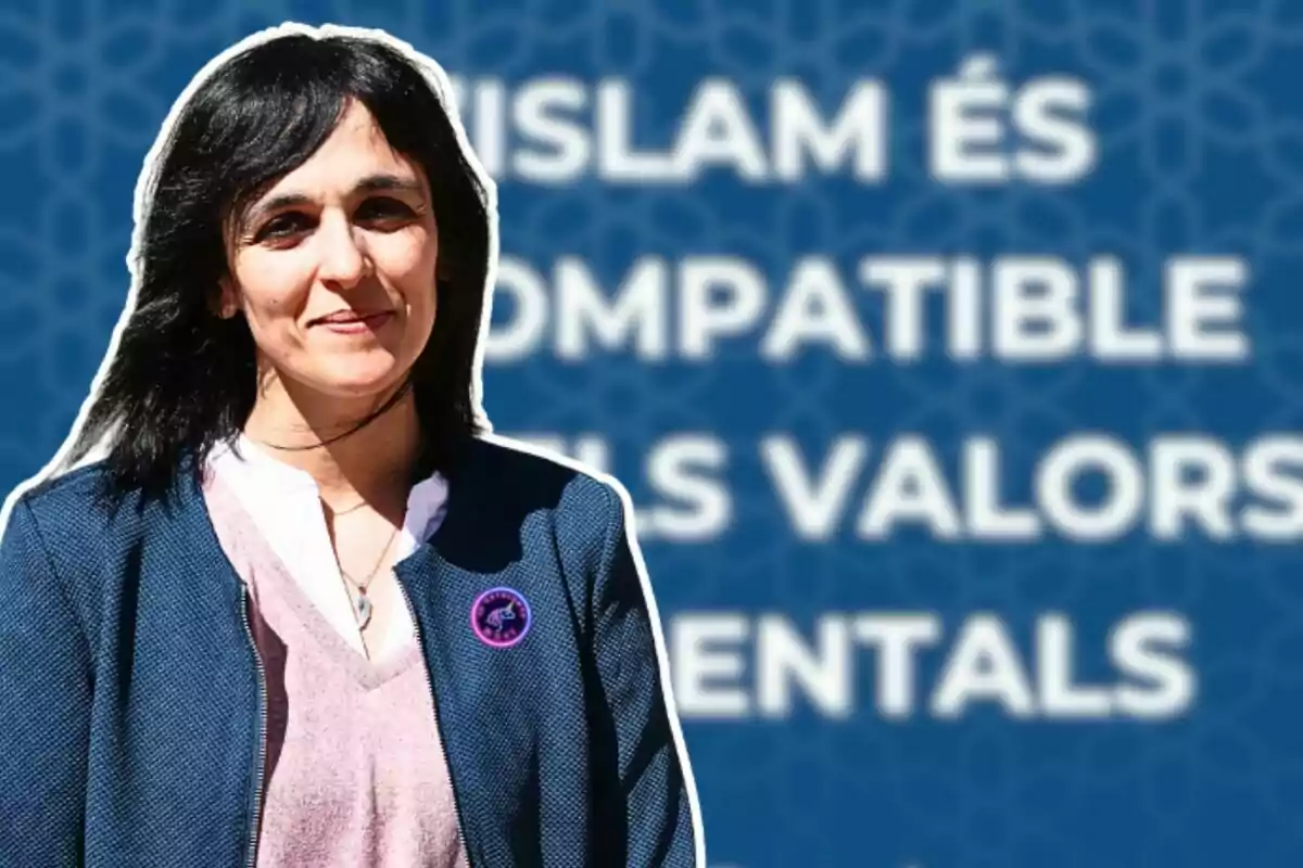 Una dona amb cabell fosc i una jaqueta blava està dreta davant d'un fons blau amb text en blanc que diu “ISLAM ÉS COMPATIBLE ELS VALORS MENTALS”.