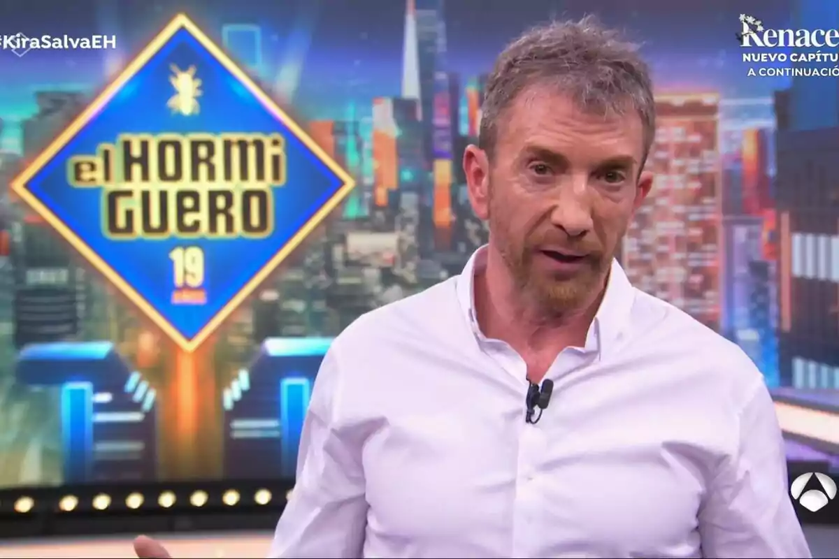 Pablo Motos amb camisa blanca està parlant en un programa de televisió anomenat “El Hormiguero” amb un fons colorit i urbà.