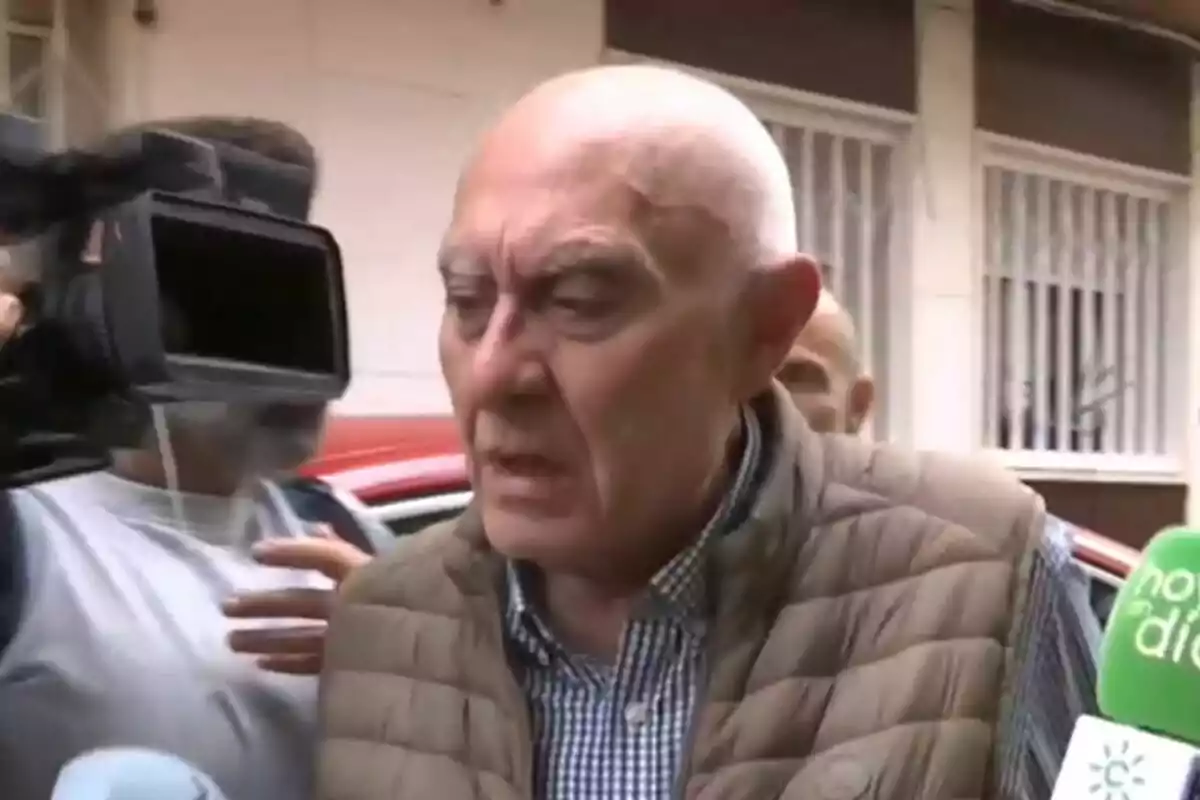 Un home gran amb armilla marró és entrevistat per diversos mitjans de comunicació al carrer. Un home gran amb armilla marró és entrevistat per diversos mitjans de comunicació al carrer.