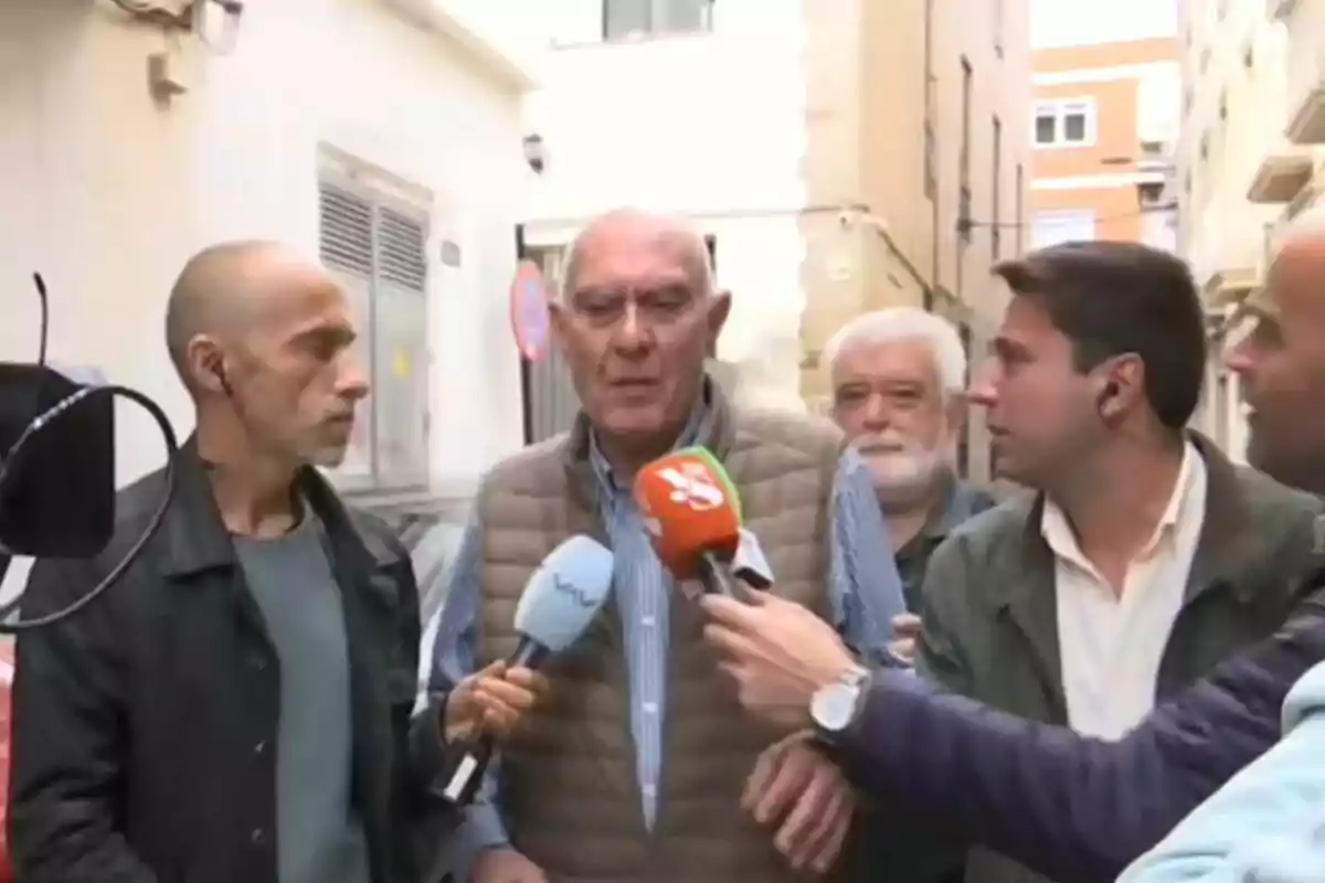 Un grup de persones està sent entrevistat per diversos periodistes en un carrer estret, amb micròfons de diferents mitjans de comunicació apuntant cap a ells. Un grup de persones està sent entrevistat per diversos periodistes en un carrer estret, amb micròfons de diferents mitjans de comunicació apuntant cap a ells.