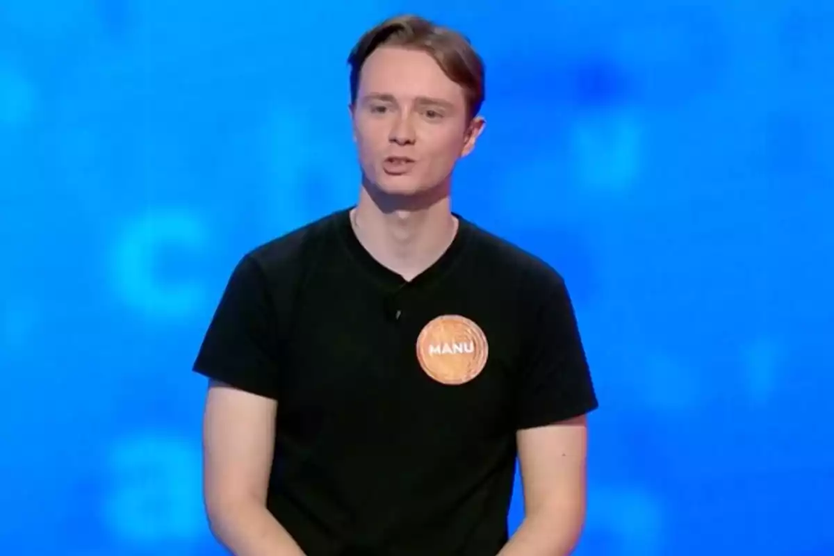 Manu wearing a black jersey and a name tag that says Manu against a blue background. Screenshot from 'Pasapalabra' Manu wearing a black jersey and a name tag that says Manu against a blue background. Screenshot from 'Pasapalabra'