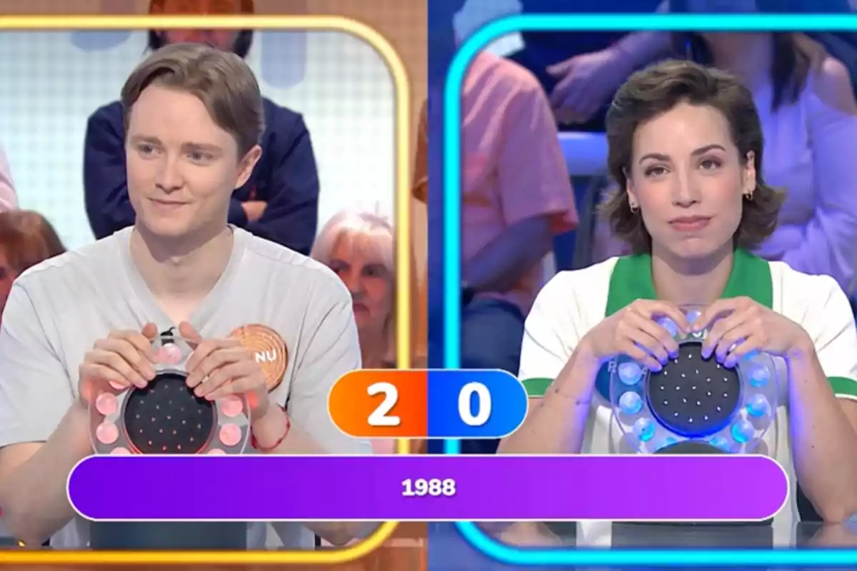 Manu and Rosa are participating in a quiz show, each holding a buzzer, and the scoreboard shows 2 to 0 with the year 1988 on the screen. Screenshot from 'Pasapalabra' Manu and Rosa are participating in a quiz show, each holding a buzzer, and the scoreboard shows 2 to 0 with the year 1988 on the screen. Screenshot from 'Pasapalabra'