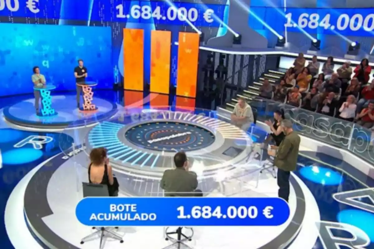 TV game show with contestants on a modern set, audience in the background, and a jackpot of €1,684,000 displayed on screen. Screenshot from 'Pasapalabra' TV game show with contestants on a modern set, audience in the background, and a jackpot of €1,684,000 displayed on screen. Screenshot from 'Pasapalabra'
