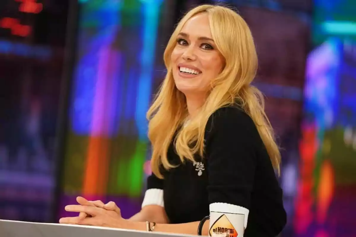 Patricia Conde rossa somrient asseguda a 'El Hormiguero' amb un fons colorit i una tassa d''El Hormiguero' sobre la taula