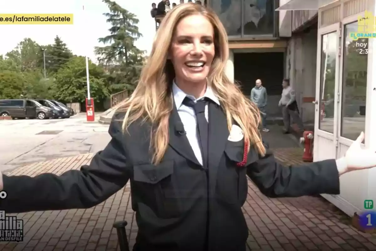 Paula Vázquez somrient amb uniforme fosc i corbata està a l'aire lliure, amb els braços oberts, mentre diverses persones i vehicles es veuen al fons en l'estrena de La Família de la Tele. Paula Vázquez somrient amb uniforme fosc i corbata està a l'aire lliure, amb els braços oberts, mentre diverses persones i vehicles es veuen al fons en l'estrena de La Família de la Tele.