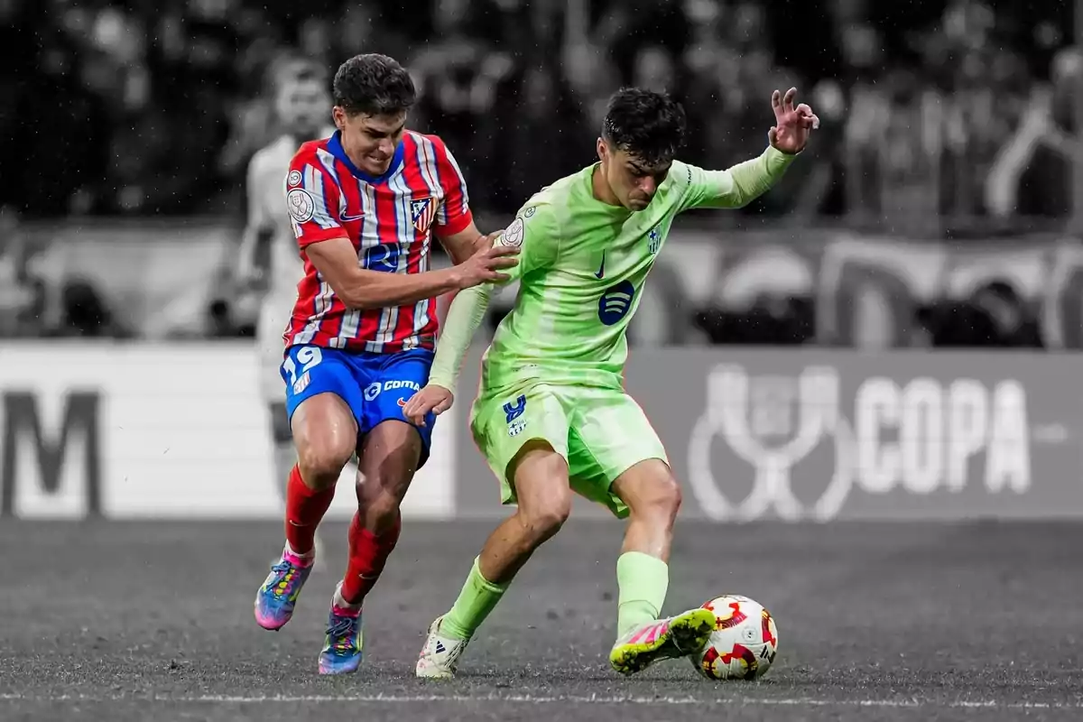 Dos jugadores de fútbol compiten por el balón en un partido, uno con uniforme a rayas rojas y blancas y el otro con uniforme verde claro. Dos jugadores de fútbol compiten por el balón en un partido, uno con uniforme a rayas rojas y blancas y el otro con uniforme verde claro.