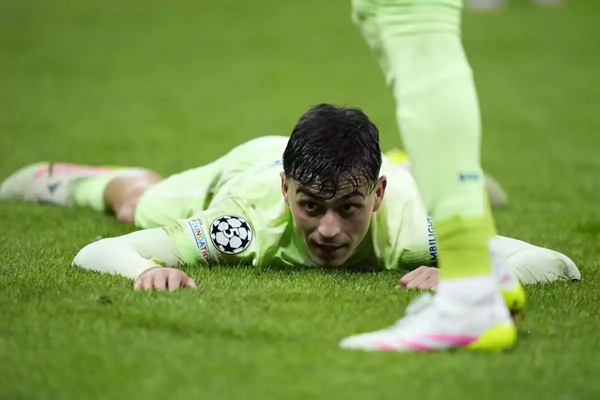 Un jugador de futbol amb uniforme verd clar està estirat a la gespa durant un partit. Un jugador de futbol amb uniforme verd clar està estirat a la gespa durant un partit.