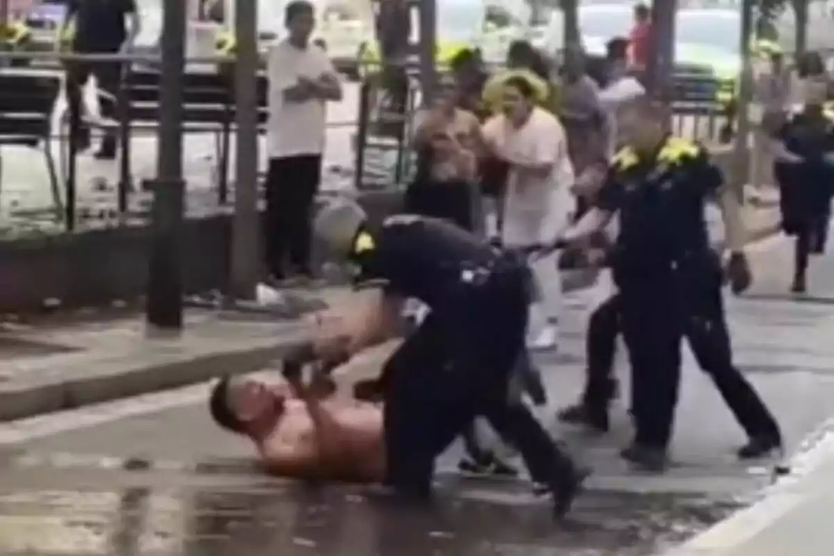 Un home sense camisa està sent sotmès a terra per un policia mentre altres oficials i persones observen l?escena en un carrer.