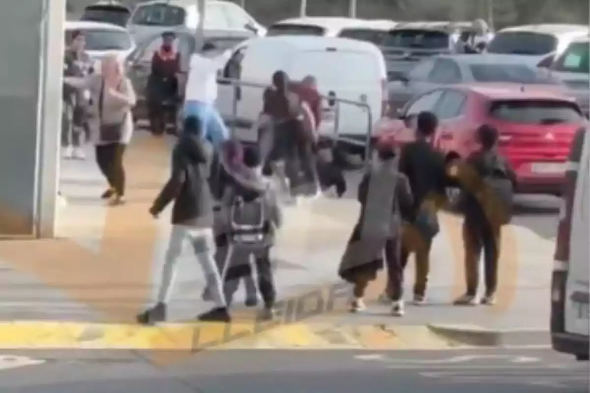 Un grupo de personas camina por un estacionamiento lleno de vehículos, mientras algunas parecen interactuar entre sí.