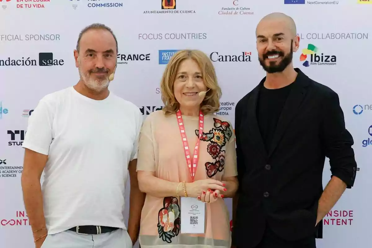 Montse Besada, Gorka García i Oriol Sala-Patau posen somrients davant d’un fons amb logotips de patrocinadors i col·laboradors en un esdeveniment