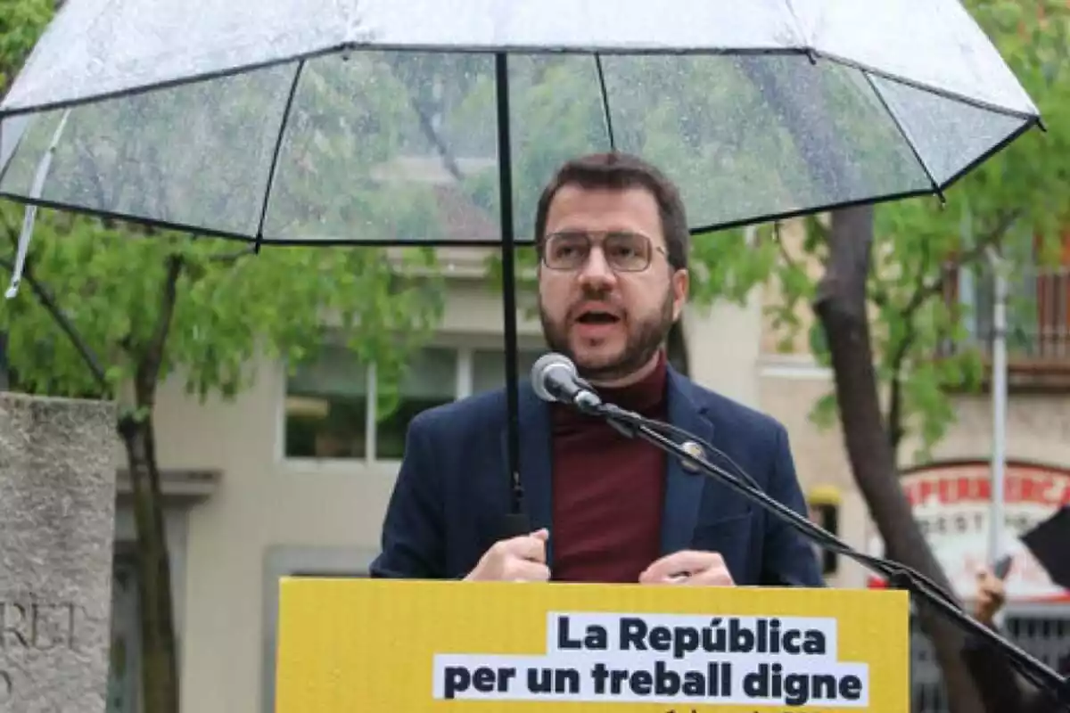 Fotografia de Pere Aragonès en un míting aguantant un paraigua sota la pluja