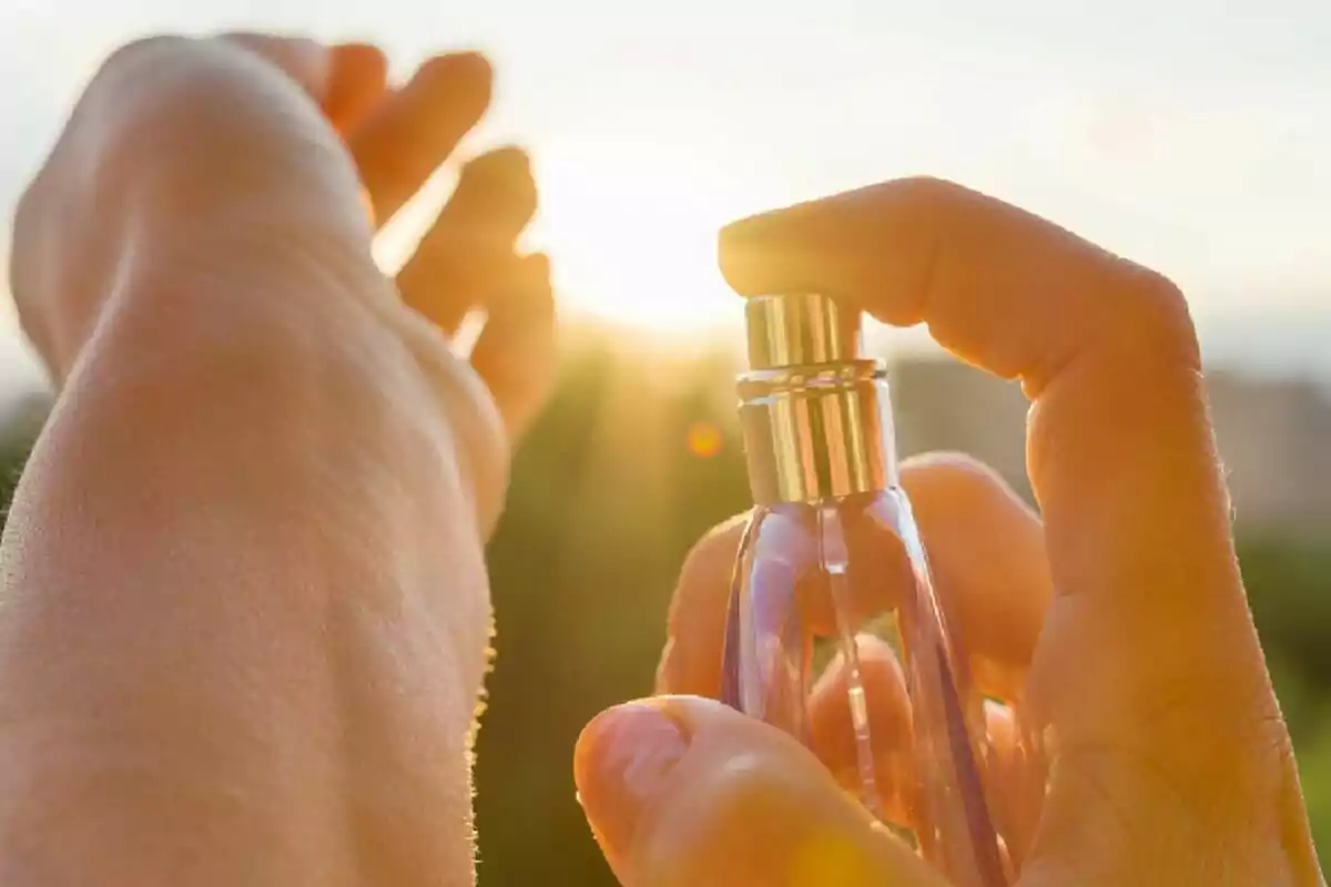 Una persona aplicando perfume en su muñeca al aire libre con el sol de fondo.