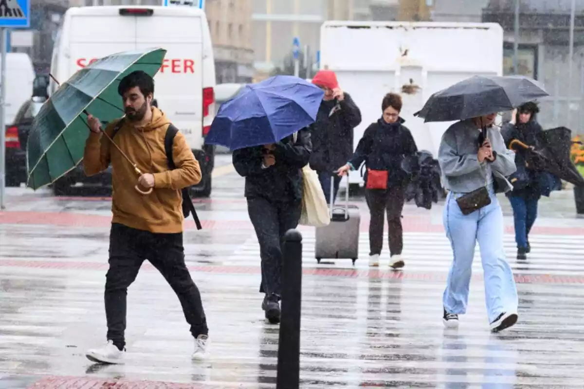 Diverses persones creuant un carrer amb paraigües en un dia de pluja a Santander