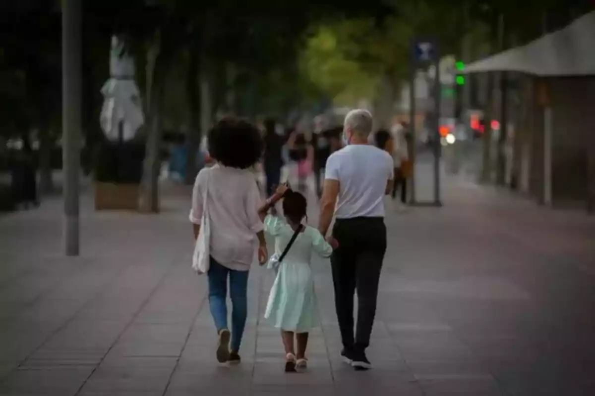 Una família caminant de la mà per un carrer arbrat al capvespre.