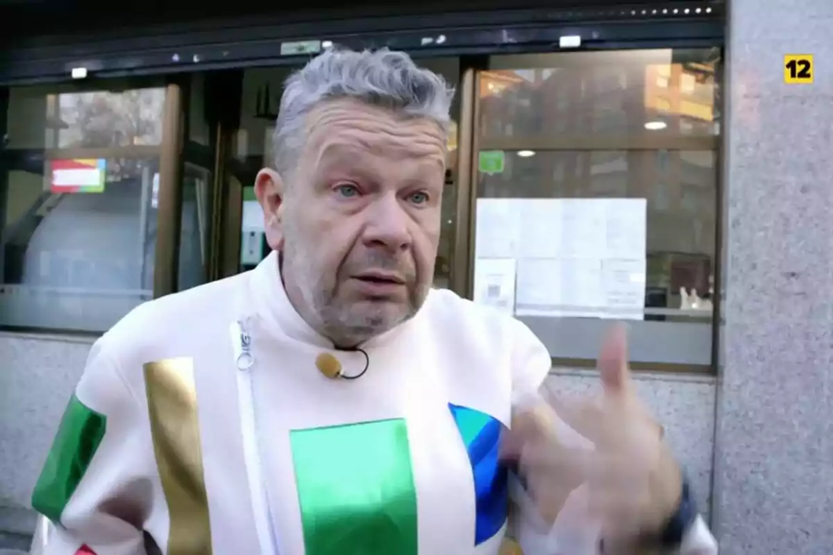 Alberto Chicote amb jaqueta blanca i detalls de colors parlant davant d'un restaurant de Malson a la Cuina.