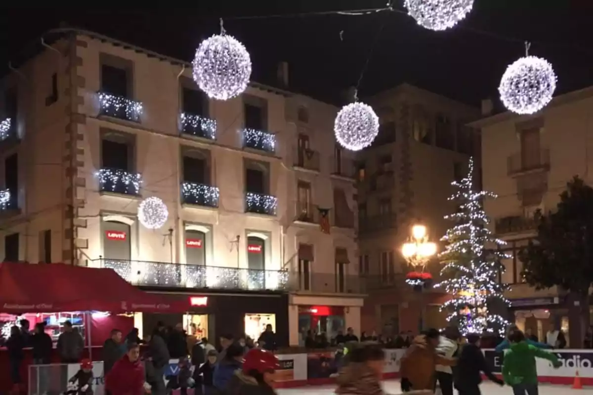 Persones patinant sobre gel en una plaça decorada amb llums nadalenques i esferes brillants penjants.