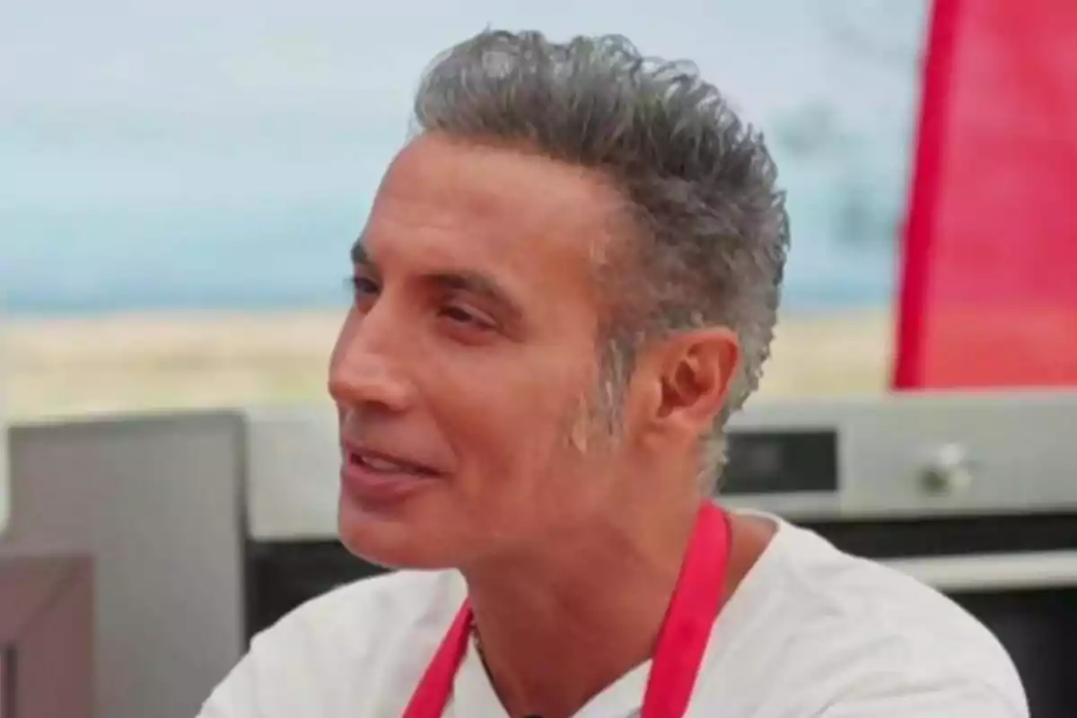 Pitingo amb cabell canós i curt porta un davantal vermell mentre somriu en un entorn a l'aire lliure a MasterChef Celebrity.