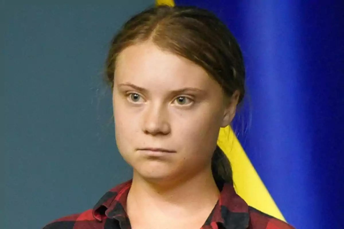 Greta Thunberg amb expressió seriosa i cabells recollits davant d’un fons blau i groc. Greta Thunberg amb expressió seriosa i cabells recollits davant d’un fons blau i groc.