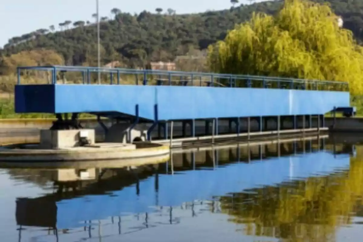 Una estructura blava sobre un cos daigua amb turons i arbres al fons.