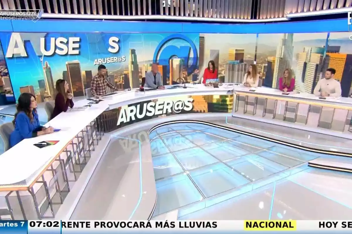 Un grupo de colaboradores como Tatiana Arús, Marc Redondo, Alfonso Arús, Angie Cárdenas o Hans Arús está sentado alrededor de una mesa en un set de televisión con un fondo de ciudad y el logo de 