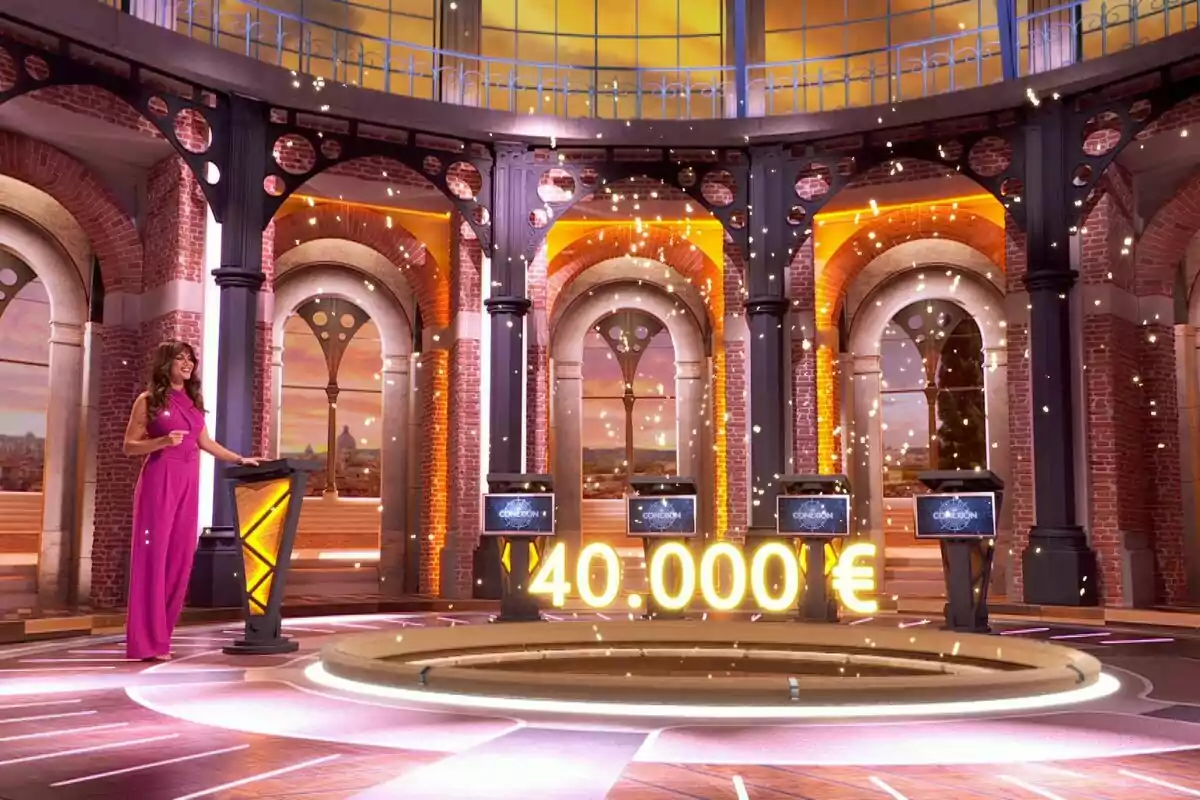 Lara Álvarez amb vestit rosa està dreta en un plató de concurs il·luminat amb llums daurades i un premi de 40.000 euros destacat al centre a 'La Conexió'. Lara Álvarez amb vestit rosa està dreta en un plató de concurs il·luminat amb llums daurades i un premi de 40.000 euros destacat al centre a 'La Conexió'.