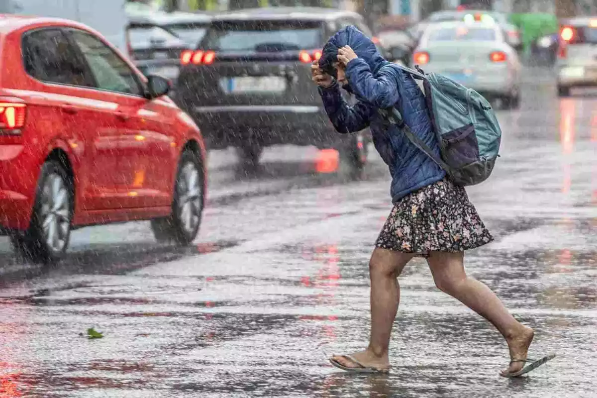 Imatge d'una dona, amb jaqueta i xancletes, escapant-se de la pluja a València