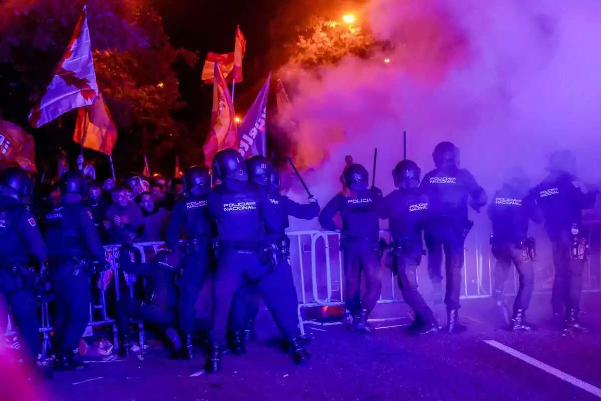 Diversos policies antiavalots intenten calmar amb les porres els centenars de manifestants que hi ha darrere d'unes tanques