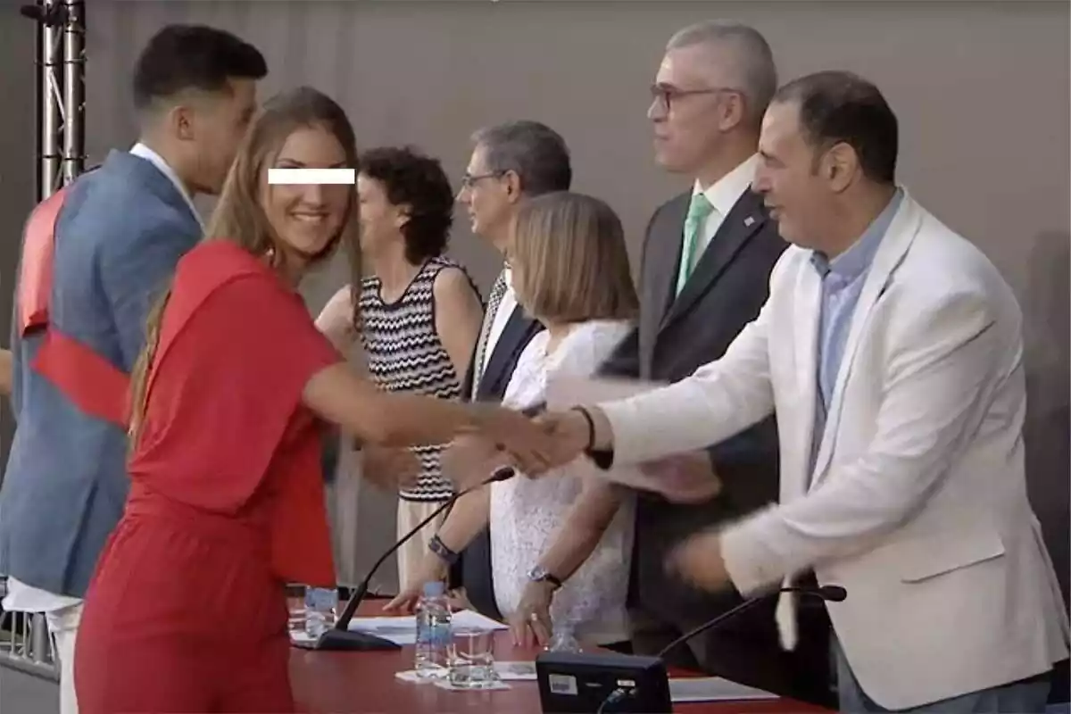 Pla americà de Maria, la policia infiltrada en el moviment indepe, recollint el seu diploma de graduada mentre mira somrient a càmera amb un vestit vermell
