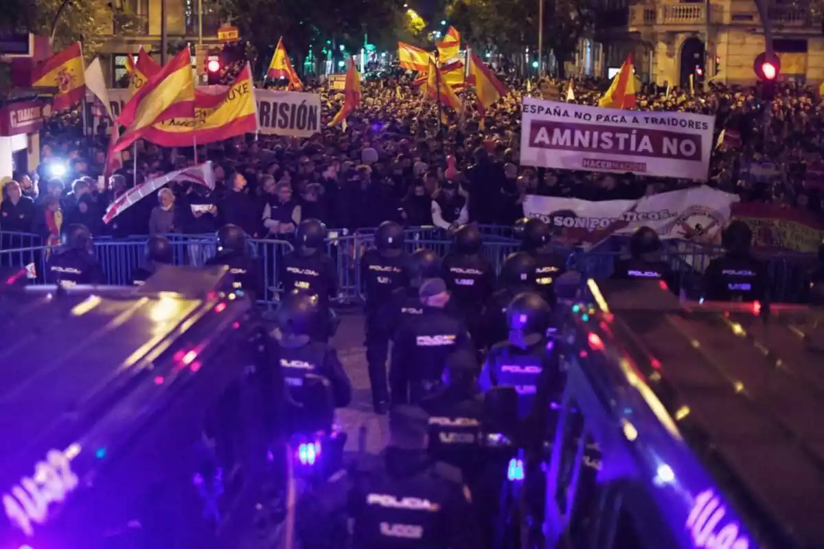 Pla general del cordó policial davant del carrer Ferraz de Madrid i al davant, milers de manifestants amb banderes espanyoles i pancartes contra Pedro Sánchez i l'amnistia