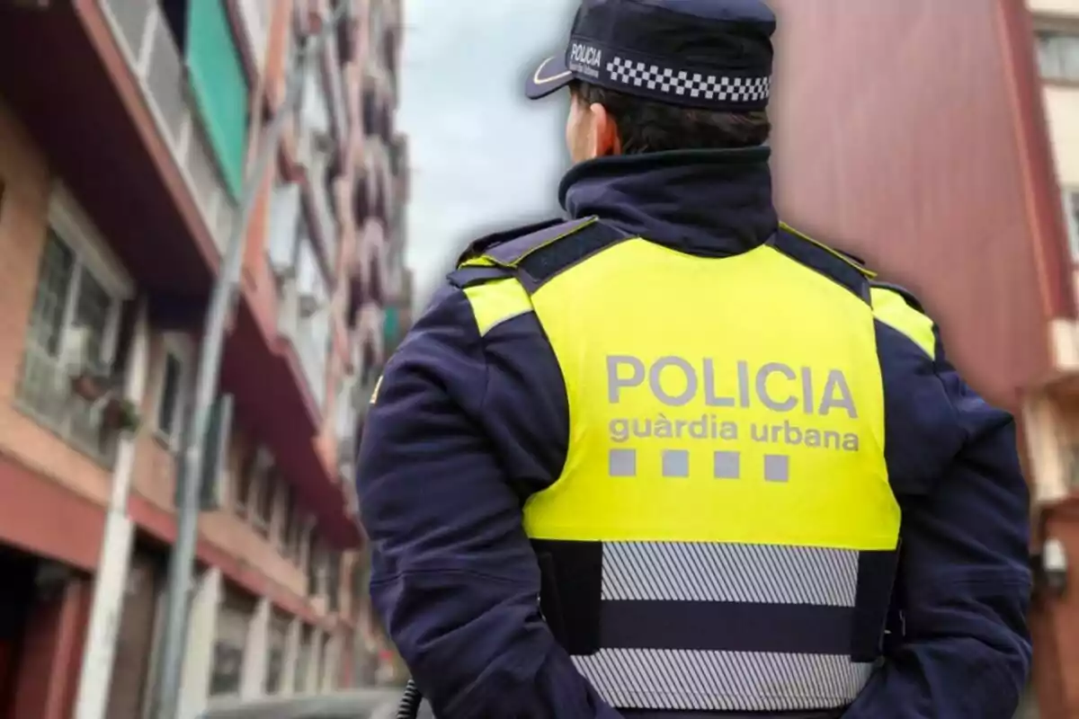 Un agente de la guardia urbana con chaleco amarillo de espaldas en una calle urbana.