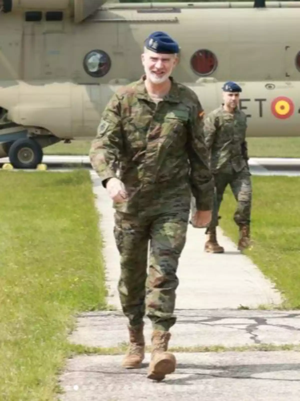 Felip VI i un altre home amb uniforme de camuflatge i boina blava caminen per una pista de formigó amb un helicòpter militar de fons. Felip VI i un altre home amb uniforme de camuflatge i boina blava caminen per una pista de formigó amb un helicòpter militar de fons.