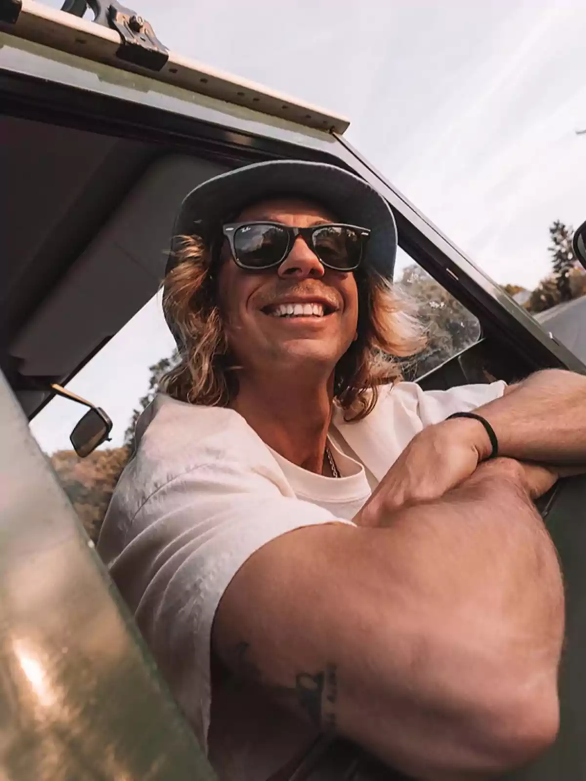 Luis Giménez, smiling with sunglasses and a hat, leans out the window of a vehicle. Luis Giménez, smiling with sunglasses and a hat, leans out the window of a vehicle.