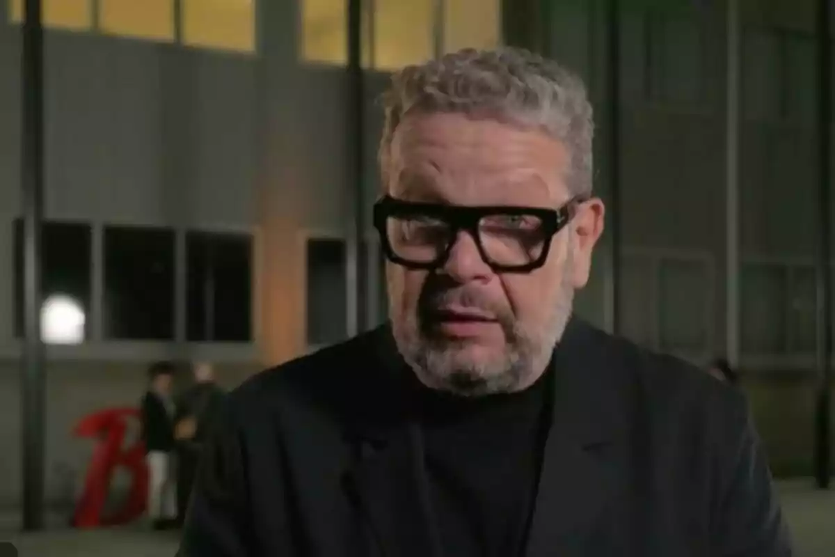 Alberto Chicote con gafas negras y barba está de pie frente a un edificio iluminado por la noche.