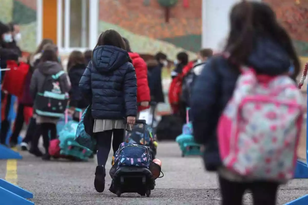 Imatge de diversos nens a l'exterior d'una escola entrant amb les motxilles