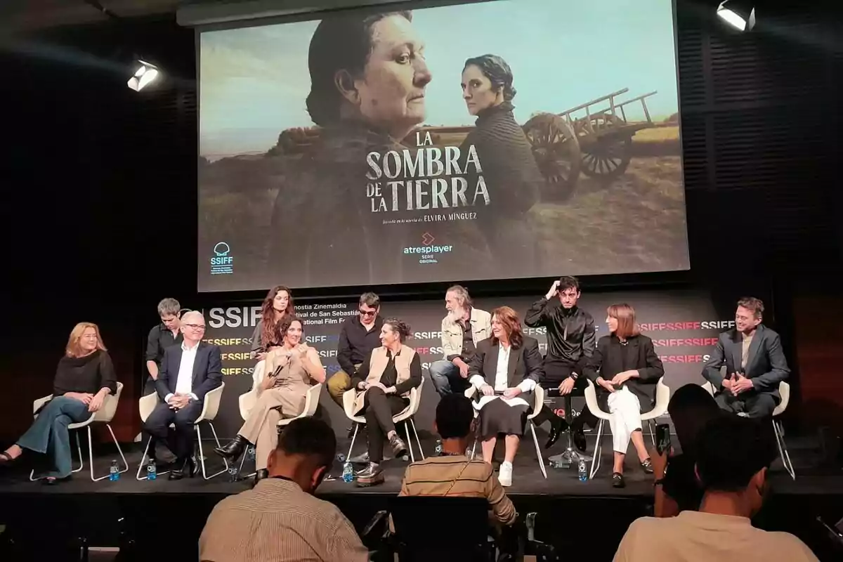 Un grup de persones com Elvira Mínguez, Adelfa Calvo, Maria Morales, Ginés García Millán, Montse García o Emilio Sánchez Zaballos està assegut en un escenari al Festival de Sant Sebastià durant una conferència de premsa, amb un cartell de la pel·lícula "L'Ombra" de la Terra" projectat a la pantalla darrere d'ells.