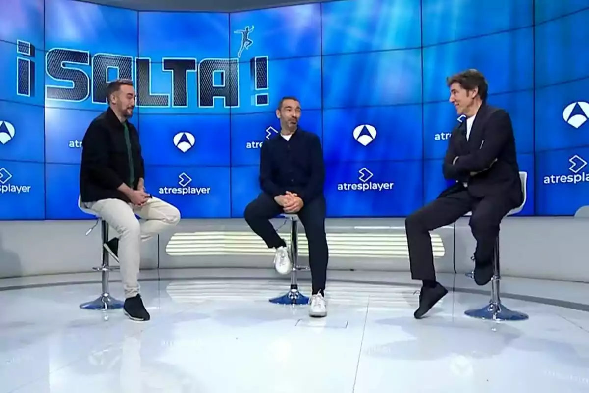 Carlos F. Recio, Jonathan Ruiz i Manel Fuentes estan asseguts en tamborets en un plató de televisió amb un fons blau que mostra el logotip d'Antena 3 i Atresplayer i la paraula "¡SALTA!".