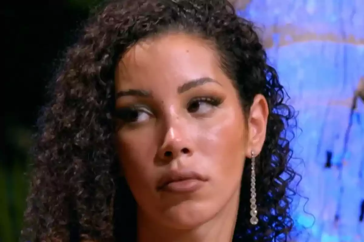 Woman with curly hair and a serious expression wearing a long earring.