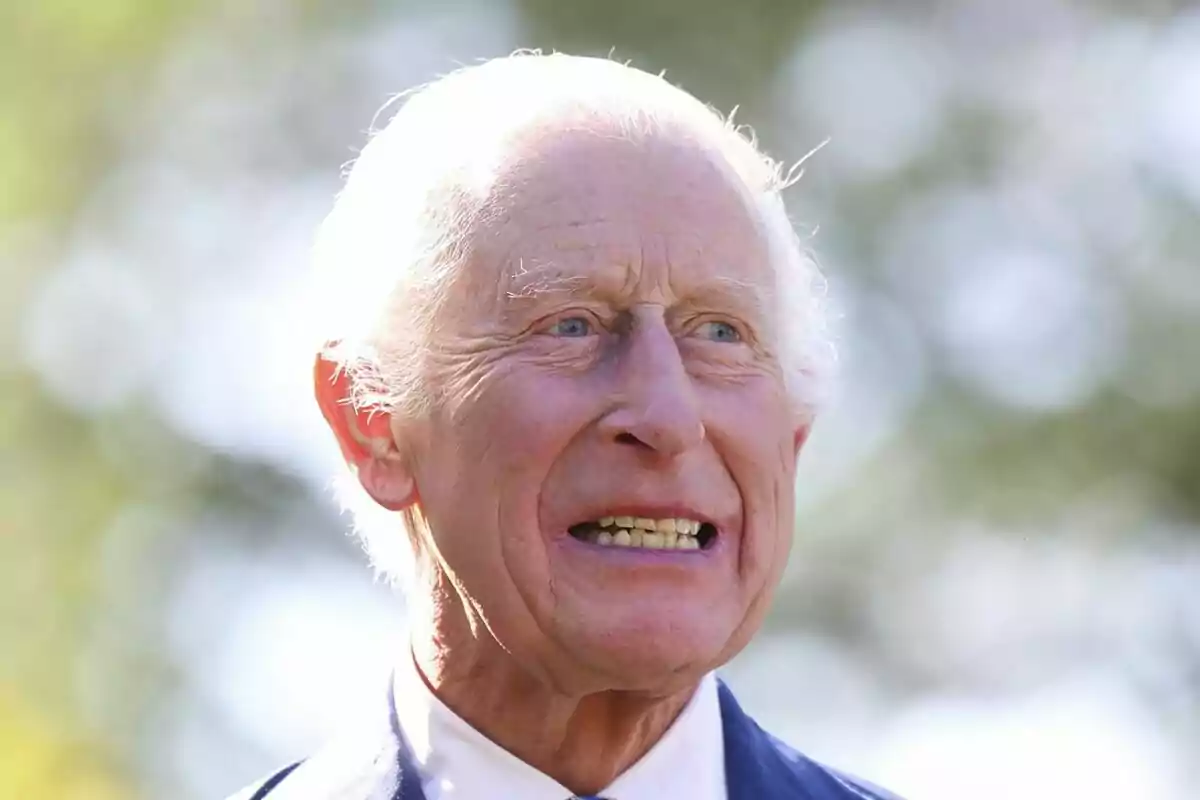 Charles III with white hair and intense facial expression in an outdoor setting with out-of-focus background.