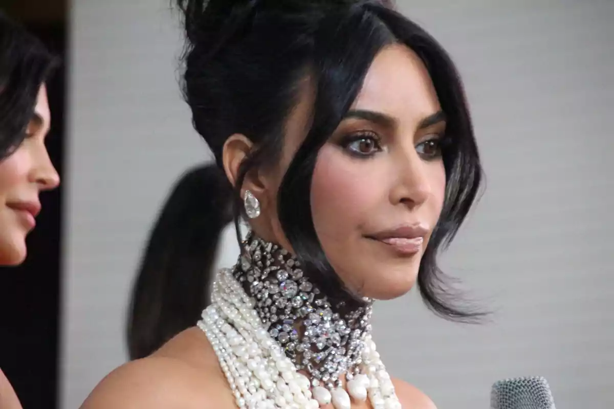 Kim Kardashian con un elaborado collar de perlas y joyas, cabello oscuro recogido y maquillaje elegante.