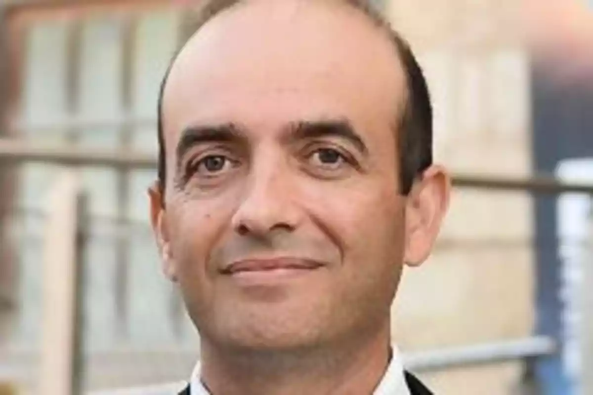 Omar Hatamleh con traje sonríe ligeramente frente a un fondo desenfocado.