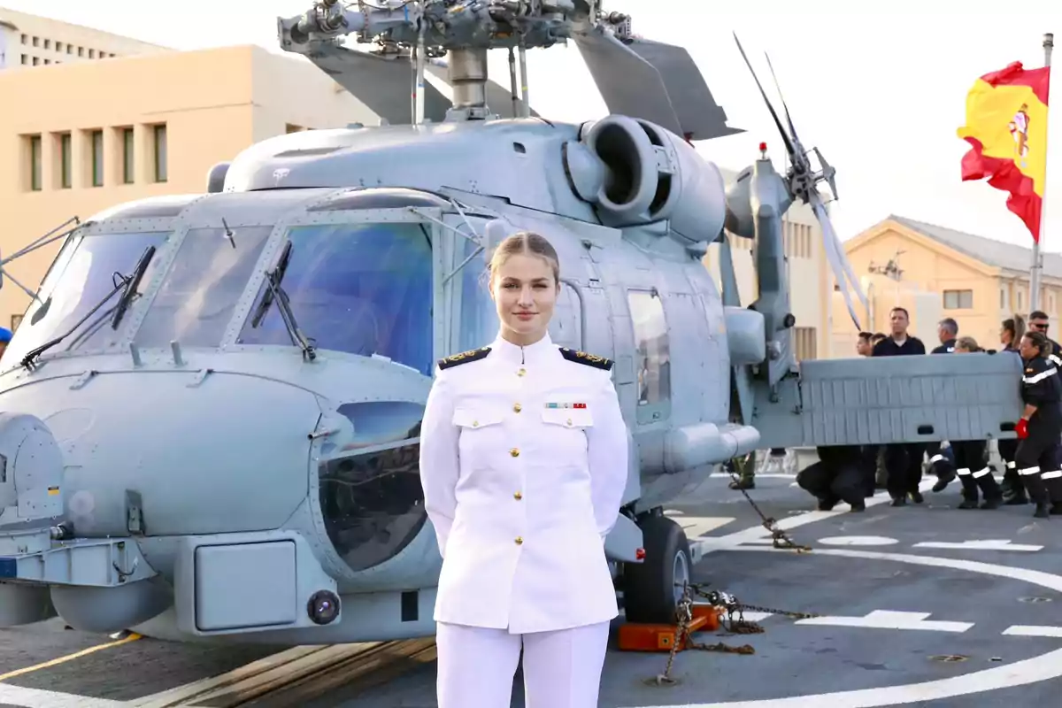 Leonor amb uniforme militar blanc de gala posant davant d’un helicòpter en una base naval amb la bandera d’Espanya al fons Leonor amb uniforme militar blanc de gala posant davant d’un helicòpter en una base naval amb la bandera d’Espanya al fons