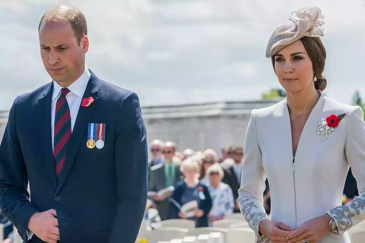 Prince William serious in a blue and red suit and tie next to Kate Middleton dressed in white with a headdress