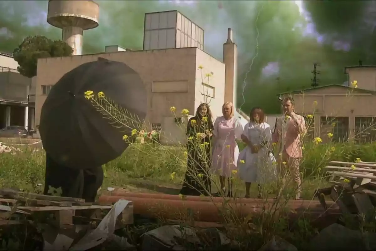 Un grup de persones format per Inés Hernand, María Patiño, Belén Esteban i Aitor Albizua està dret en un terreny amb vegetació i runa, mentre una figura amb un paraigua negre es troba en primer pla; al fons hi ha un edifici industrial i el cel està cobert de núvols verds amb un llamp visible en una promo de La Família de la Tele. Un grup de persones format per Inés Hernand, María Patiño, Belén Esteban i Aitor Albizua està dret en un terreny amb vegetació i runa, mentre una figura amb un paraigua negre es troba en primer pla; al fons hi ha un edifici industrial i el cel està cobert de núvols verds amb un llamp visible en una promo de La Família de la Tele.