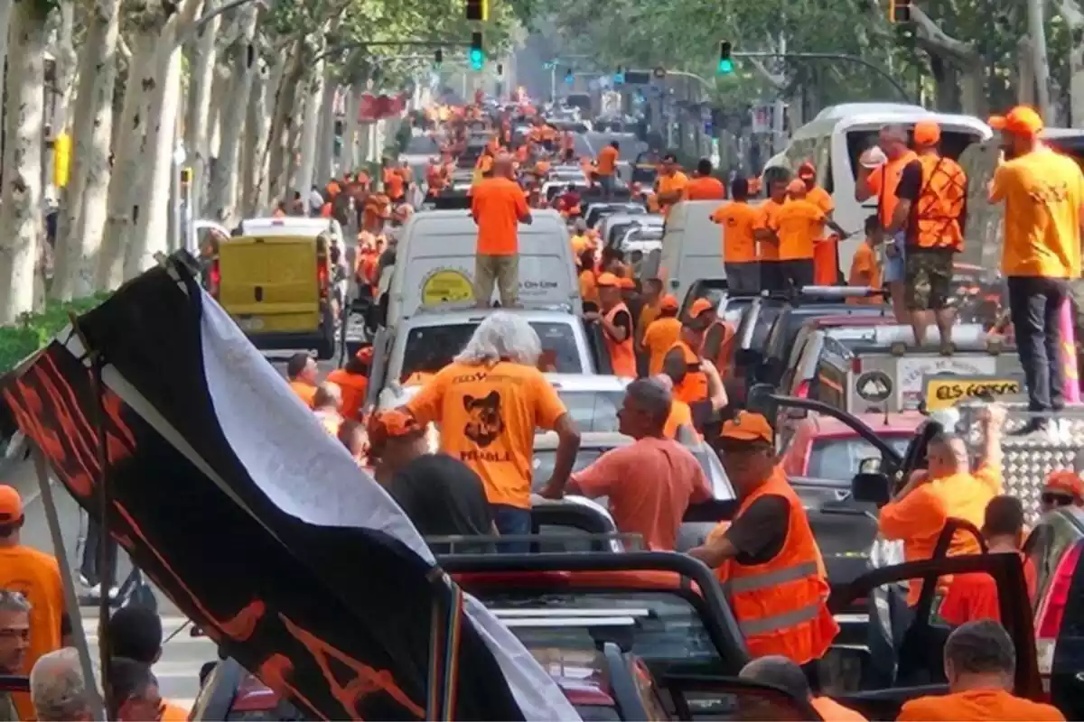 Pla general de desenes de caçadors manifestant-se a Barcelona amb samarretes taronges i pujats a cotxes que col·lapsen la circulació