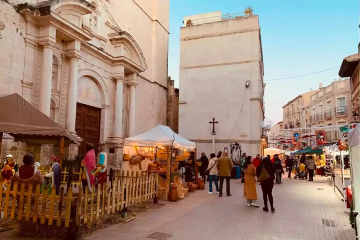 Un carrer amb un mercat exterior al costat d'una església antiga, amb persones passejant i parades de venda il·luminades.