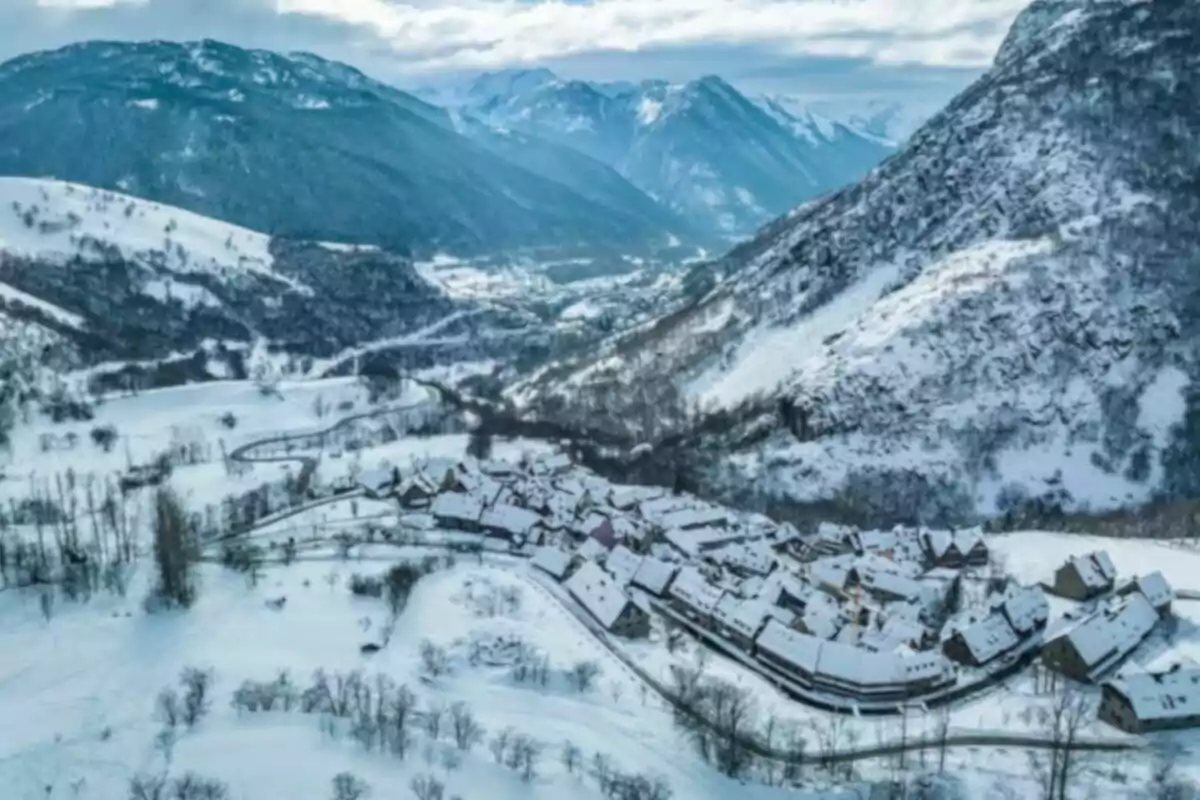 Vista aérea de un pueblo cubierto de nieve rodeado de montañas en un paisaje invernal.