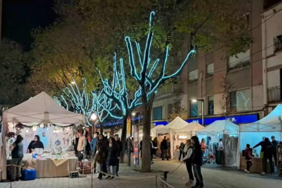 Una fira nocturna amb parades de venda il·luminades i arbres decorats amb llums blaves.