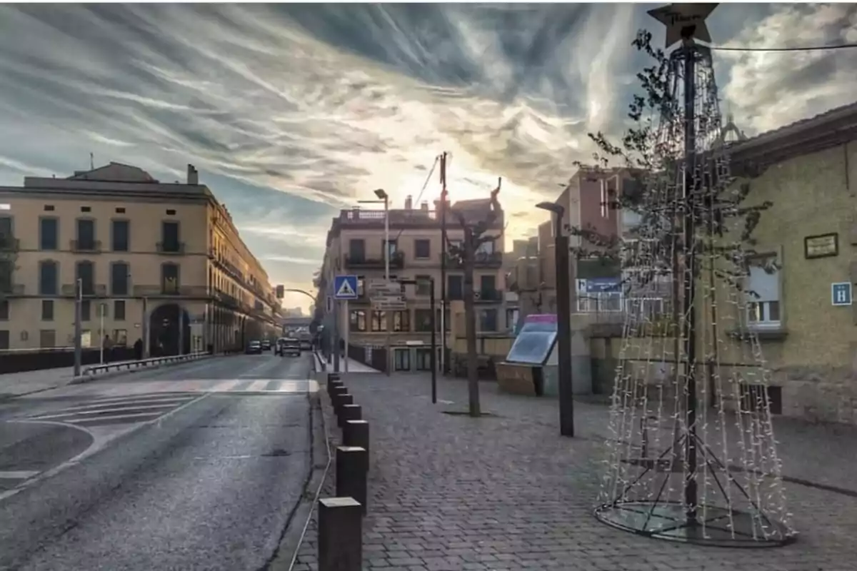 Carrer urbà amb edificis als costats i un arbre de Nadal il·luminat al capvespre.